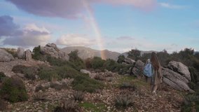 A young woman walks in the mountains. The girl looks at the rainbow over the mountains. Travel in the mountains of Turkey