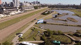 Argentinian flag waving in racecourse of Buenos Aires, with buildings of city in background, Palermo hippodrome. Aerial circling