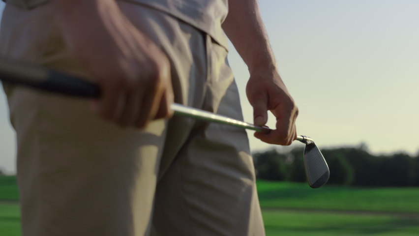 Golf player swinging club putter on sunset field. Golfer stressing on sport game. Unrecognizable man hands holding golfing equipment on course fairway. Luxury hobby wealthy lifestyle activity concept.
