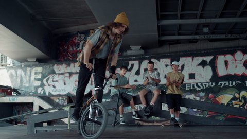 Sporty guy performing jump trick on bmx bike at skate park. Young friends applauding after jump stunt on bmx bicycle outdoors. Active people meeting on skate park. Friendship extreme sport concept. 