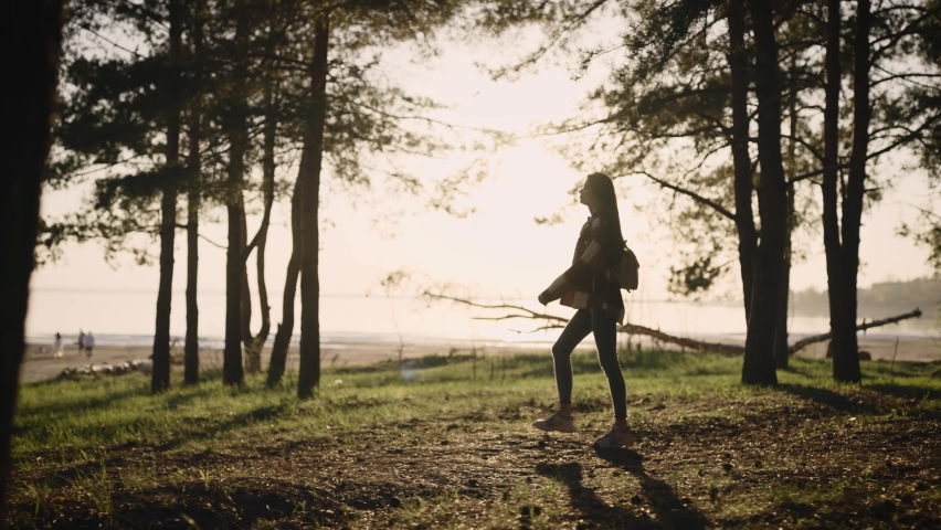 Beautiful young hipster woman in a shirt walking through a picturesque pine forest.