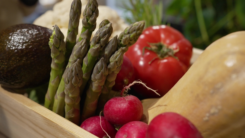 Female hand in rubber gloves puts ripe avocado in wooden box filled with fresh vegetables. Organic vegetables sorted in wooden box extreme closeup