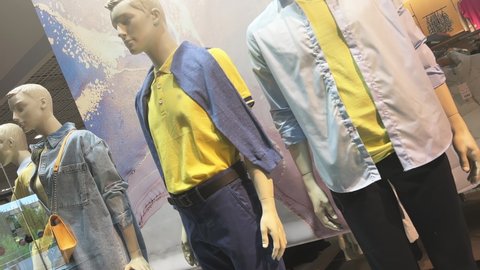 Mannequins stand in the window of a clothing store or boutique. Dutch angle
