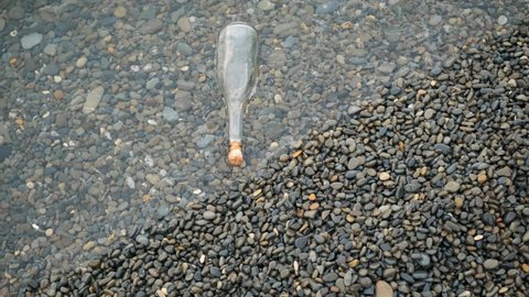 Top down view on glass bottle with wooden cork on sea or ocean. concept of note for posterity thrown into water. vintage glass bottle lies on stone beach.