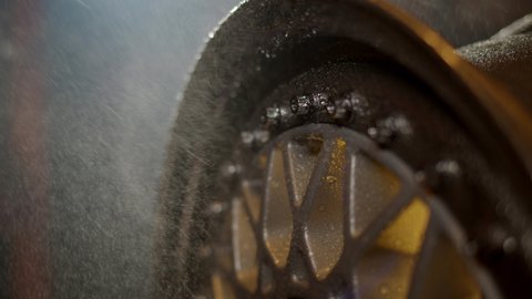 Water falls on beautiful freshly painted rim from car with water drops on polished shelves and bolts. Classic wheel close up on background of garage in defocus.