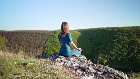 Relaxed peaceful yogi woman sitting in lotus while meditating, feeling free in front of wild nature. Mindful fitness coach having zen moment. Everyday yoga practice, calm breath, concentration concept