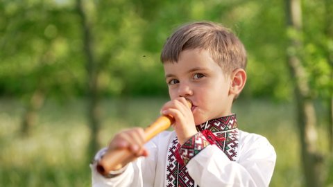 Adorable boy playing on woodwind wooden flute - ukrainian sopilka. Folk music concept. Musical instrument. Kid in traditional embroidered shirt - Vyshyvanka.