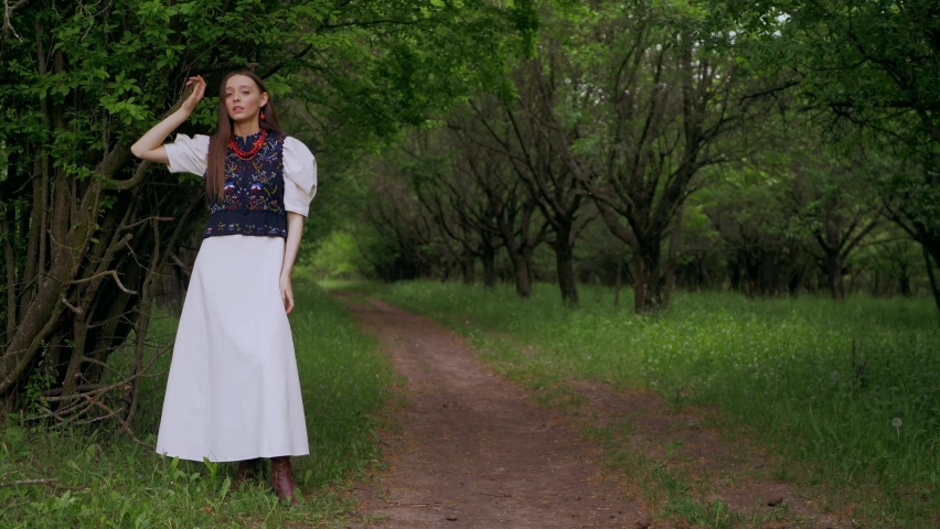 Ukrainian girl in a green garden. Beautiful woman in an embroidered dress walks in the park.