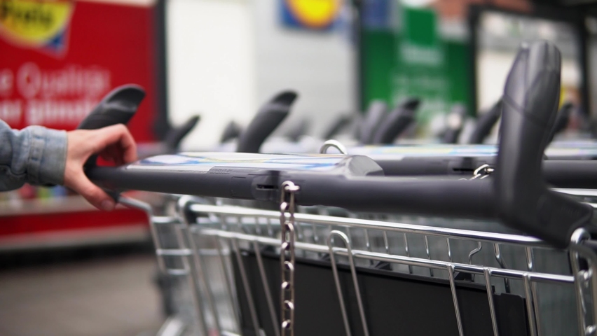 Shot of a women wearing a blue jeans jacket using a 1€ coin into to rent out a shopping cart at a grocery store in germany to buy food, drinks, fruits and other stuff