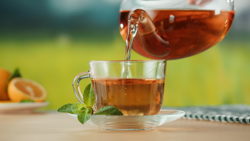 Pouring citrus tea in cup close-up. Fresh hot herbal tea with mint and oranges, healthy morning, detox drink.