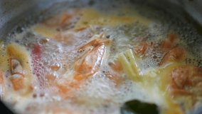 Top view video 4k of spicy prawn soup or Tom Yum Kung In a boiling pot, chili, lemongrass, kaffir lime leaves, garlic float on the surface with the steam of clear sour and spicy soup.