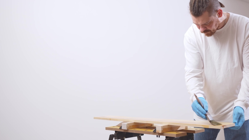 the carpenter covers the wood with oil with a brush. decorative and protective varnish or liquid wax for the processing of wood products. natural wood in interior design.