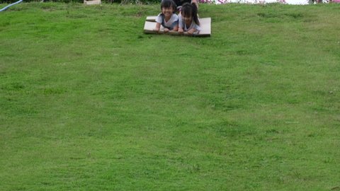 Two smiling little sisters lie prone on cardboard boxes sliding down the hill at the Botanical Gardens. The famous outdoor learning center of Mae Moh Mine Park, Lampang, Thailand. Happy childhood conc