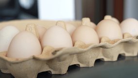 Closeup view 4k stock video footage of many fresh raw eggs from farmer. Eggs isolated in special carton egg box or package standing on table in kitchen. Woman takes pack of eggs then puts it back