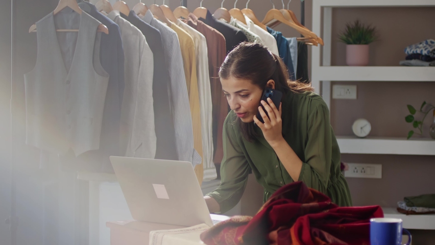 A modern Indian Asian woman or female working busy professional fashion designer is on a mobile phone call talking having a conversation with a customer. independent business, shop, store   concept | Shutterstock HD Video #1090719869