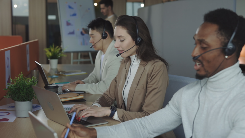 Smiling female operator answering to client query in headset while working in modern call center with multiracial colleagues. Business people, customer support and technology concept. - Powered by Shutterstock - Get 15% off with code: PIKWIZARD15