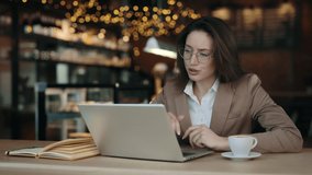 Angry business woman sitting at cafe table and having serious conversation via video call. Furious female boss using modern laptop for remote work.
