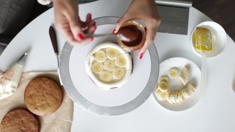 Homemade banana and caramel cake preparing process, girl's hand adding sliced banana and caramel on the top layer