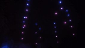 Bright colored lights move in rows in the dark night sky. Drone show.