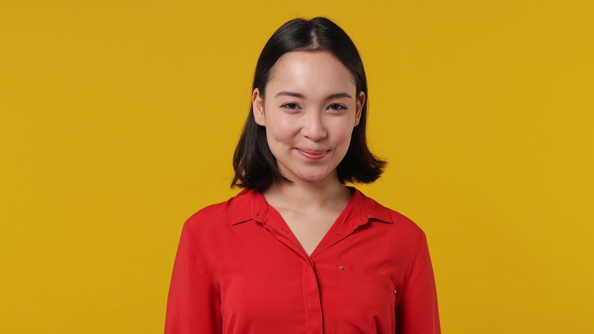 Smiling charming vivid young woman of Asian ethnicity 20s years old wears red shirt looking camera wink eye blink isolated on plain yellow background studio portrait. People emotions lifestyle concept Royalty-Free Stock Footage #1090725039