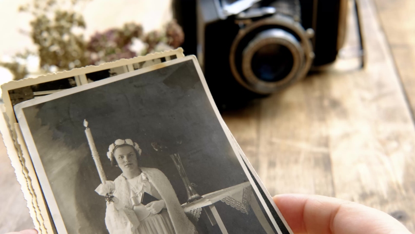female hand hold old family photos, stack of old family vintage photographs of 50s, 40s, black retro accordion camera on wooden table, concept of genealogy, memory of ancestors, family tree, memories Royalty-Free Stock Footage #1090726735