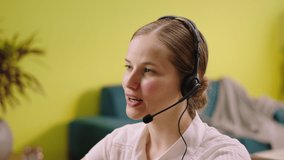At the call centre office the woman operator taking video closeup have a conversation with some customer she helps them she holding her headset
