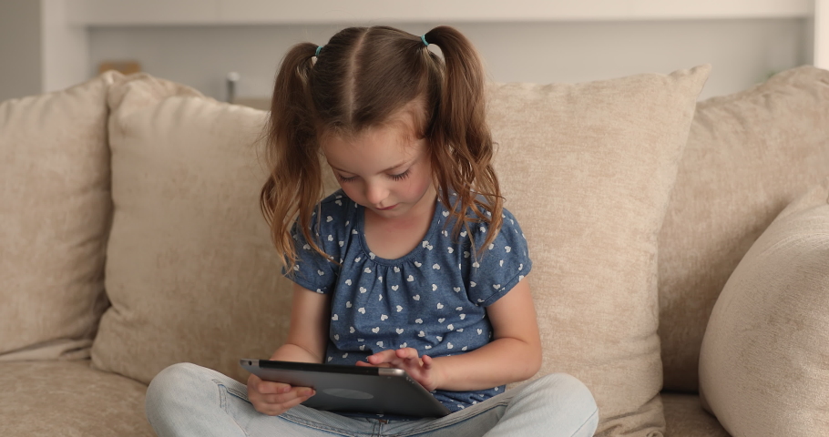 Addicted to modern technology adorable little preschool baby girl involved in using entertaining software or educational applications on digital computer tablet, playing online game alone at home. Royalty-Free Stock Footage #1090727935