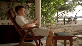 A Caucasian man puts down his phone and puts on his glasses and relaxes in a chair on the beach. The concept of working on vacation - Powered by Shutterstock - Get 15% off with code: PIKWIZARD15