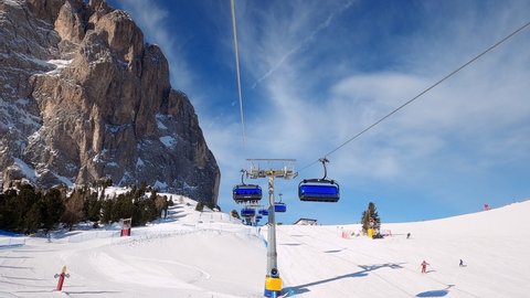 First-person view FPV point of view POV of cable chair ski lift ascend for alpine skiing in Dolomites. Ski resort piste with people skiing in Dolomites in Italy. Ski area Belvedere. Canazei, Italy