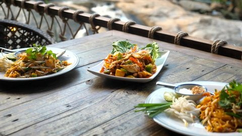 Thai traditional food in outdoor cafe. Shrimp Pad Thai, rice noodle, and sweet and sour chicken cashew nut. Asian restaurant with nature background