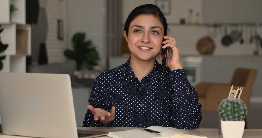 Indian businesswoman sit at desk hold smartphone make commercial offer talk to client remotely working from home due quarantine, solve business distantly use modern tech and mobile connection concept Royalty-Free Stock Footage #1090731447