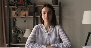 Beautiful millennial woman sit at desk pass job interview distantly using video call app concept. Female applicant wear headphones looking at camera answers questions confirm skills and qualification
