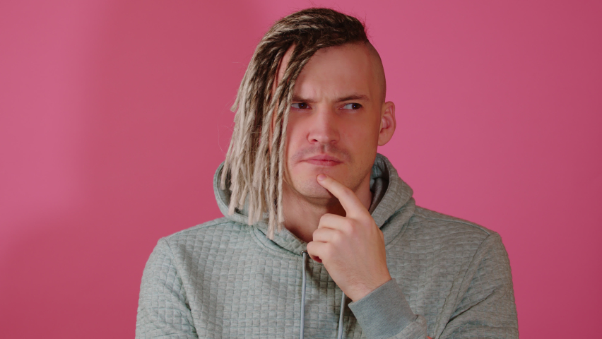 Young thoughtful handsome man with blonde dreadlocks on pink background. Pensive guy with doubt glance taps his chin with finger.
 Royalty-Free Stock Footage #1090736175