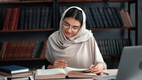 Smiling modern Muslim woman in hijab reading interesting paper book sitting at desk with laptop in public library. Arabic female student prepare to academic exam at university literary room interior - Powered by Shutterstock - Get 15% off with code: PIKWIZARD15