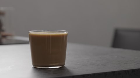 Slow motion handheld shot of milk coffee in glass on concrete countertop