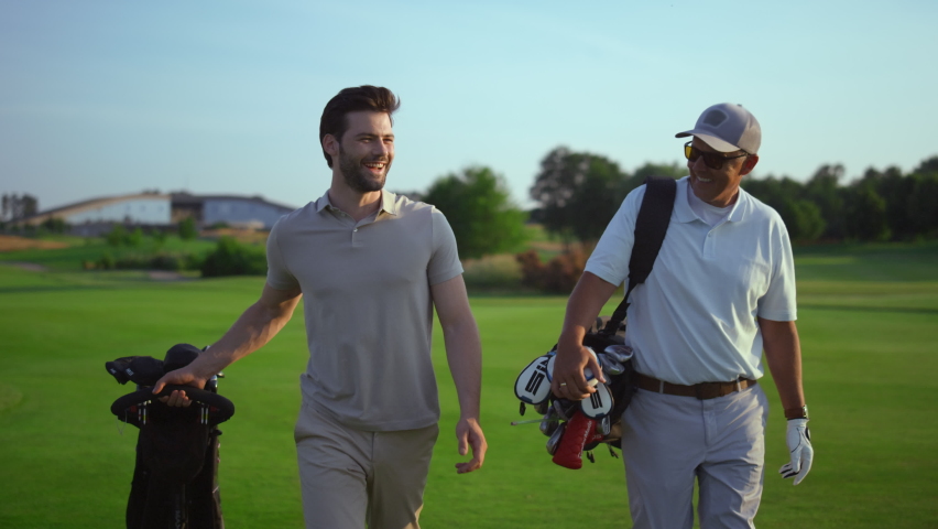 Successful golfers smiling discuss golf on course. Two men enjoy sport action on fairway. Joyful golfing players walk in countryside club on active summer weekend vacation. Friendship activity concept | Shutterstock HD Video #1090739957