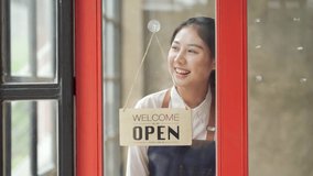 Young asian woman hanging an open sign on the window of a cafe, female owner of coffee shop or restaurant walking up to door and turning round sign to open. - Powered by Shutterstock - Get 15% off with code: PIKWIZARD15