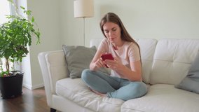 Young teenage woman using smartphone and rest on sofa at home. Relaxed teen girl student using music application online. Smiling female talking with friends in virtual chat. Technology lifestyle