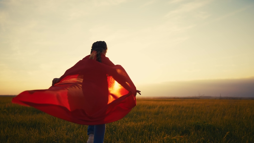 girl superhero. child in a red raincoat runs with a lifestyle dog outdoors in the park. happy family kid dream concept. little girl superhero runs with a dog across the field in nature