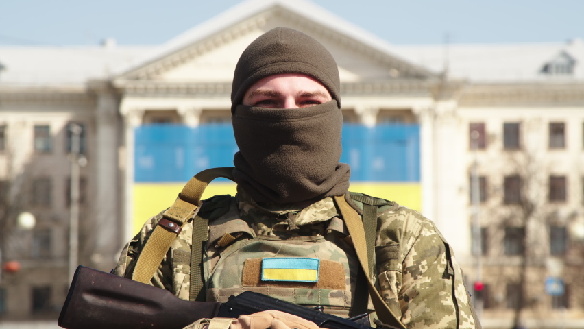 Close-up of a Ukrainian soldier in military uniform and helmet looking at the camera with the flag of Ukraine in the background.
 | Shutterstock HD Video #1090753961