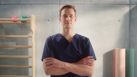 Portrait of a Handsome Professional Male Nurse Standing and Posing for Camera, Smiling in Medical Rehabilitation Center. Physiotherapy Assistant In Hospital. Young Practising Doctor.