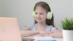Happy school girl pupil wearing wireless headphones studying online at virtual class with teacher tutor by video conference call, watching lesson on laptop computer at home. Distance learning concept