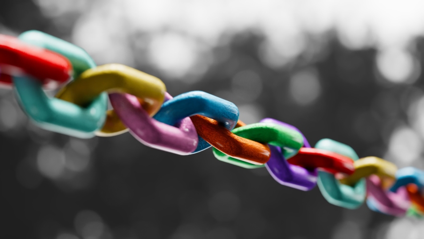 Strong multi-coloured metal chain closeup on a greyscale background. Symbol of cooperation, togetherness, diversity, variation, and teamwork. Seamless, endless looping animation.