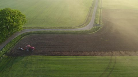 Aerial drone view of a tractor with cultivator plowing field in the early morning fog lit up the golden sunrise. Tractor disk harrow on ploughing a soil. Planting in farmland. Sowing seed on plowed