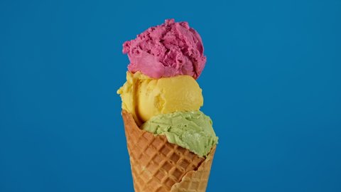 Colorful ice cream in waffle cone rotating on blue background. Delicious pink, yellow and green ice cream. Ice cream like traffic lights. Close-up of sweet dessert. 4K, UHD