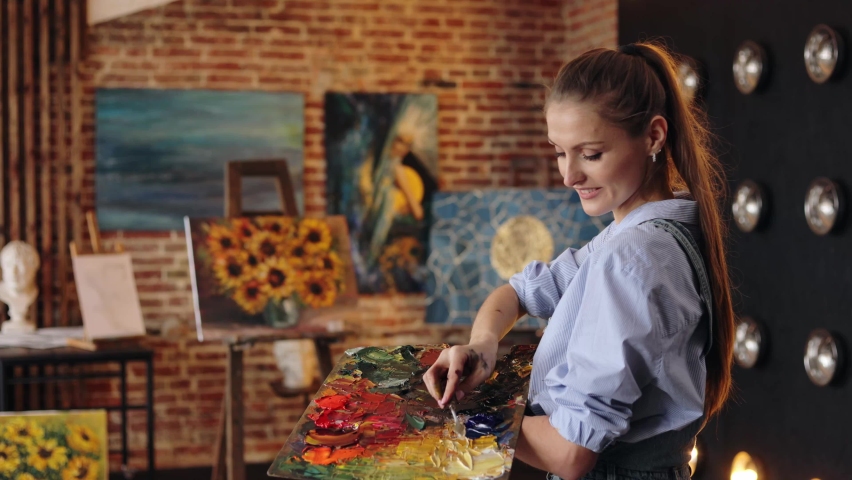 Young beautiful female artist painting still life with sunflower on canvas using oil paintings and palette knife. Painter creating artwork in art studio. Relaxation, leisure, hobby, stress management. Royalty-Free Stock Footage #1090764697