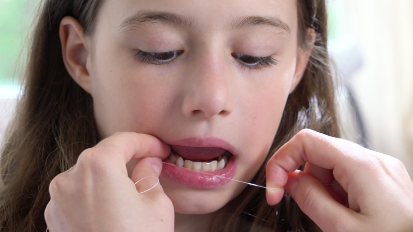 A mother pulling out a baby tooth to her little daughter using dental floss. | Shutterstock HD Video #1090765175