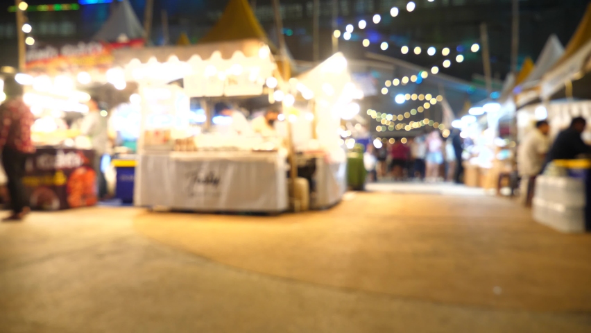 Slow motion of blurred busy busy fresh market full with crowd people walking in street shopping. Thailand street food night market booth festival light bright bokeh.