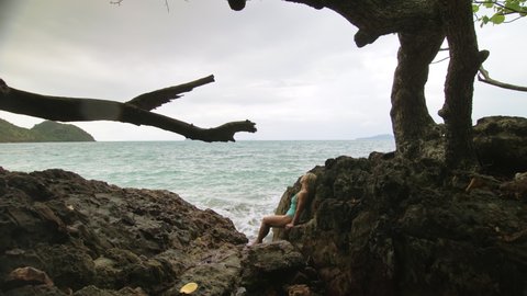 Pretty woman meditates, relaxes on rock crack reef hill in stormy morning cloudy sea. Concept feminine, sexual vaginal health, hygiene, womanly, freedom, fresh. Mother of ocean gives birth to him