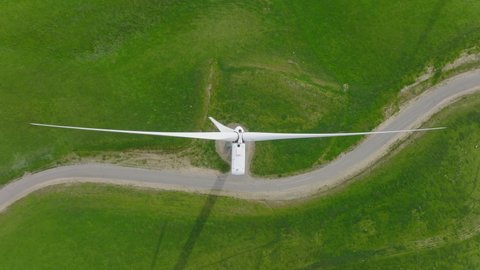 Cinematic top down aerial view of white rotating windmill blades generating renewable energy on scenic green hill. Renewable energy, sustainable development environment friendly concept 4K nature shot